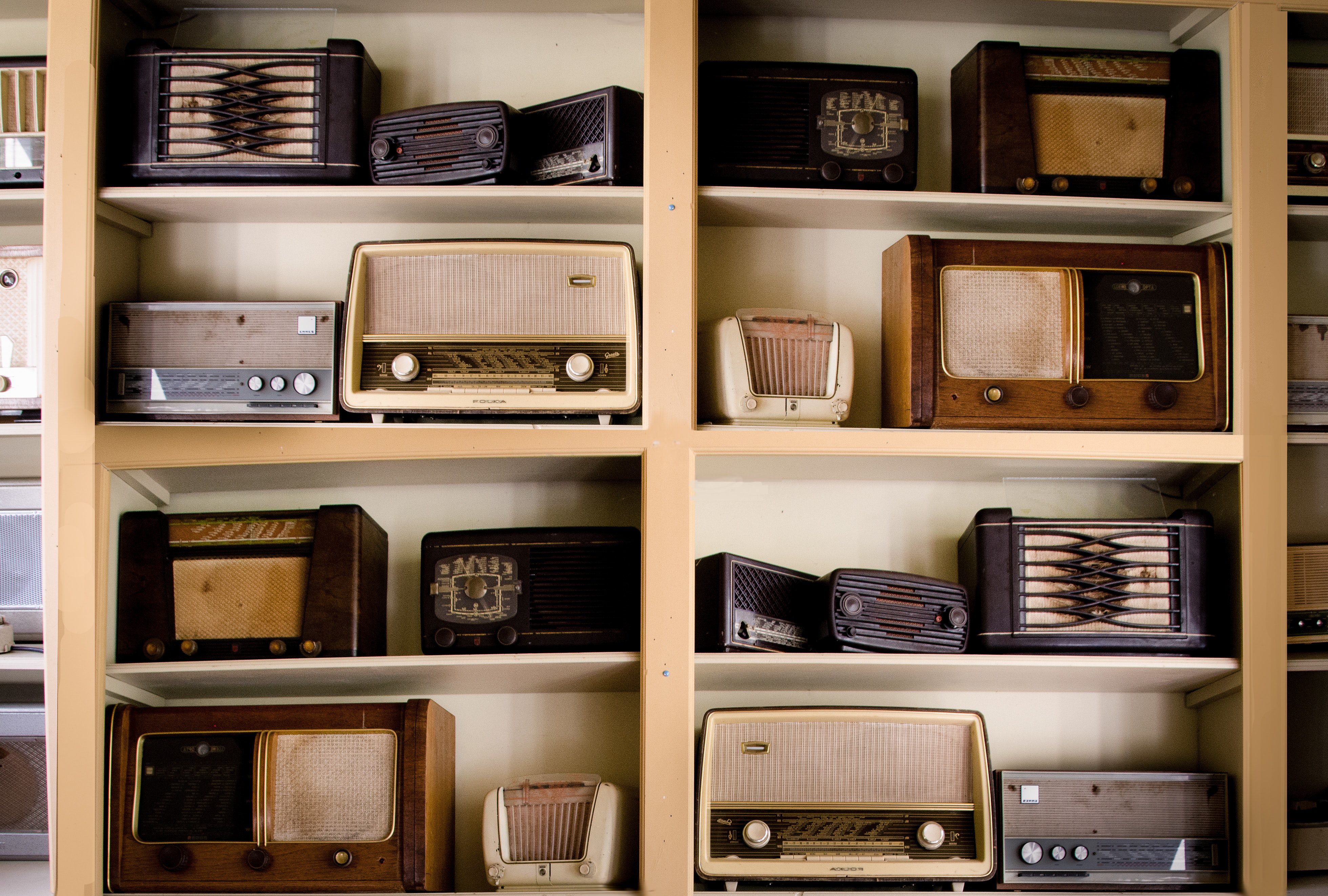 Floor to ceiling light brown book shelf fulled with brown and cream coloured vintage radios
