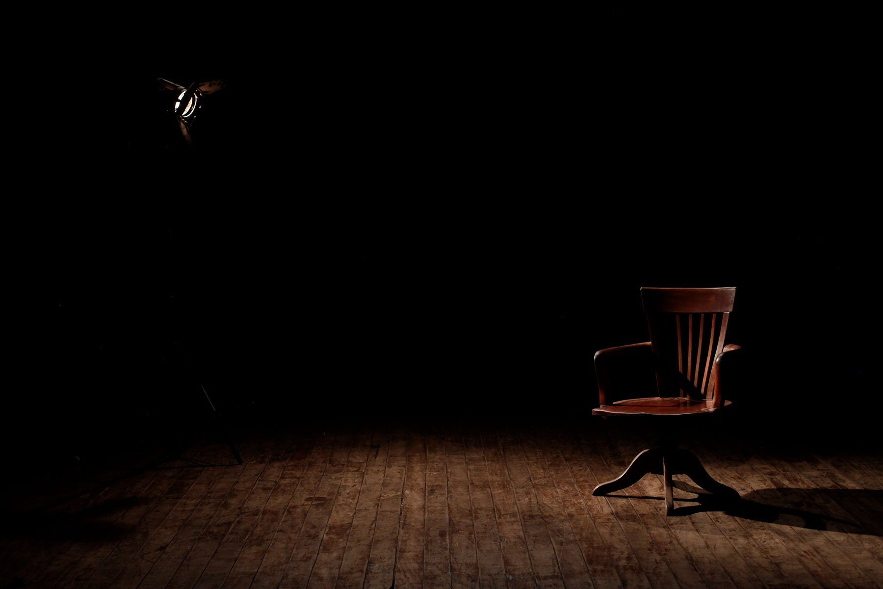 Dark empty room with one soft spot light on a Brown Wooden Armchair on a Brown Wooden Floor